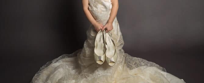 a litlte girl in her mum's wedding dress holding her bridal shoes