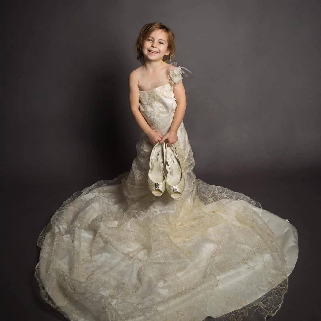 a litlte girl in her mum's wedding dress holding her bridal shoes
