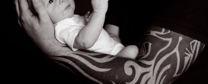 An awake newborn being held in a dad's tattooed arms - black and white