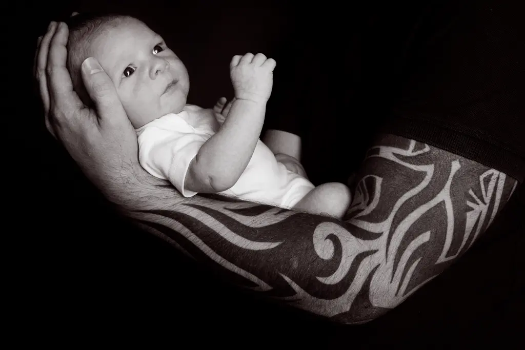 An awake newborn being held in a dad's tattooed arms - black and white