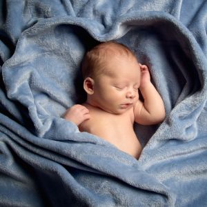A newborn sleeping in a blue blanket arranged to make the shape of a heart