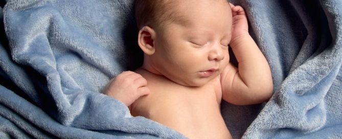 A newborn sleeping in a blue blanket arranged to make the shape of a heart
