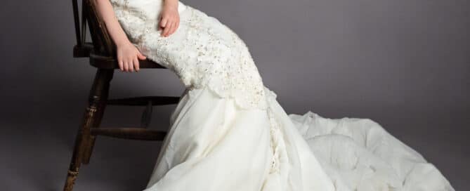 a little poses in her mums wedding dress sitting on a chair