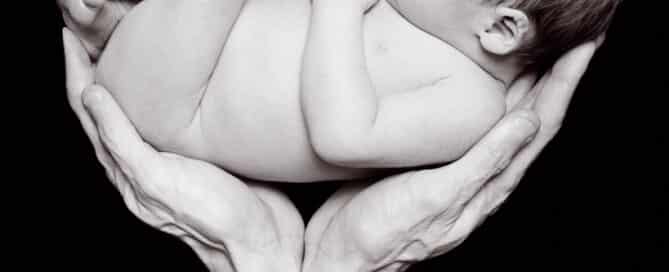 A black and white image of a sleeping newborn being supported in their father's hands