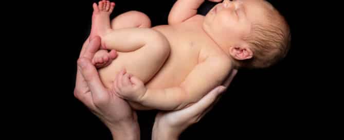 A newborn baby being supported by the hands of both parents
