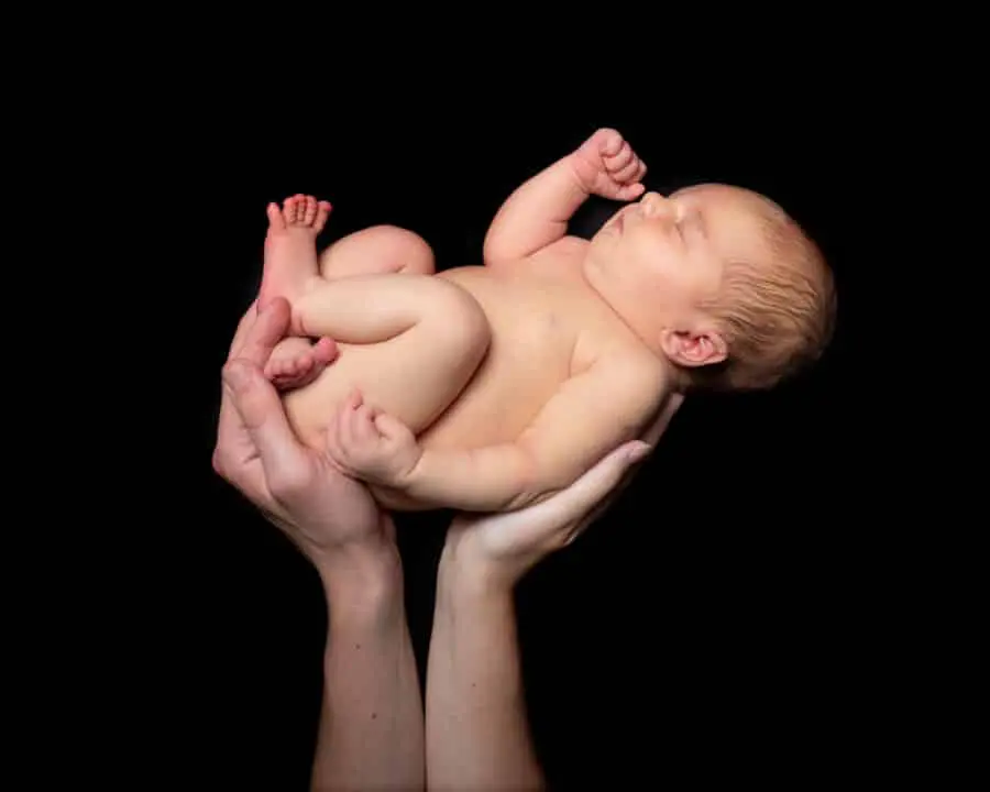 Newborn Photography East Grinstead West Sussex A newborn baby being supported by the hands of both parents