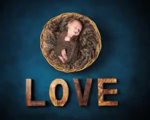 A digital image of a sleeping newborn in a basket over wooden letters that spell love