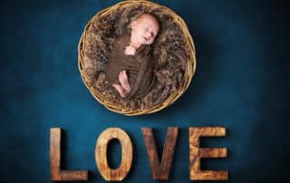 A digital image of a sleeping newborn in a basket over wooden letters that spell love