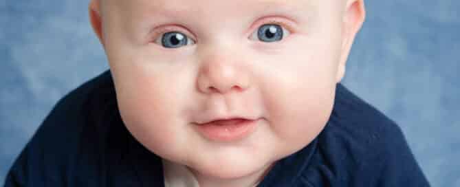 a little blue eyed boy poses on his tummy on a blue blanket looking at the camera