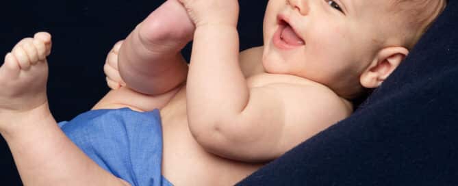 a little boy holds his feet as he lies on a navy blue blanket