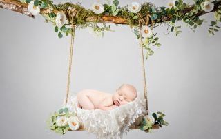 a digital image of a newborn sleeping on their tummy on a white floral swing