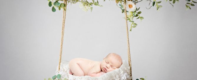 a digital image of a newborn sleeping on their tummy on a white floral swing