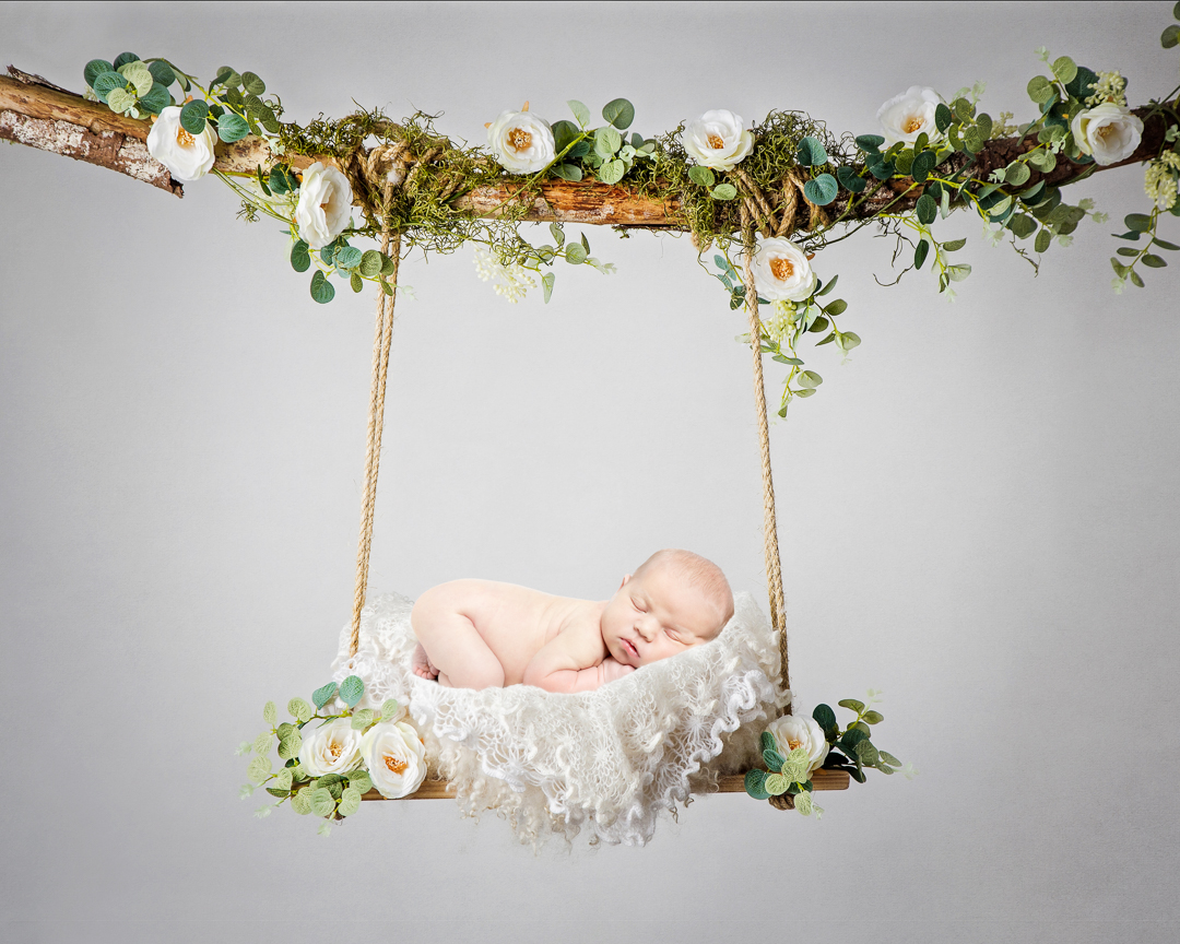 a digital image of a newborn sleeping on their tummy on a white floral swing