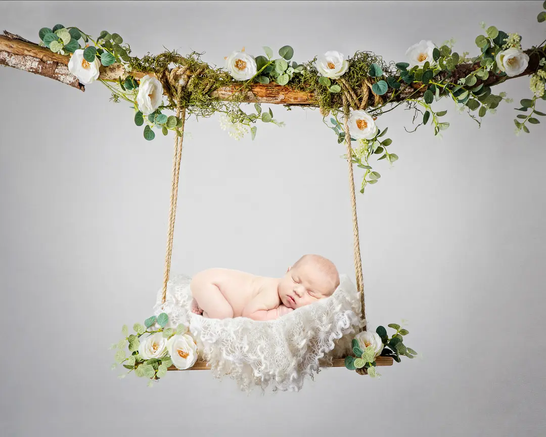 a digital image of a newborn sleeping on their tummy on a white floral swing