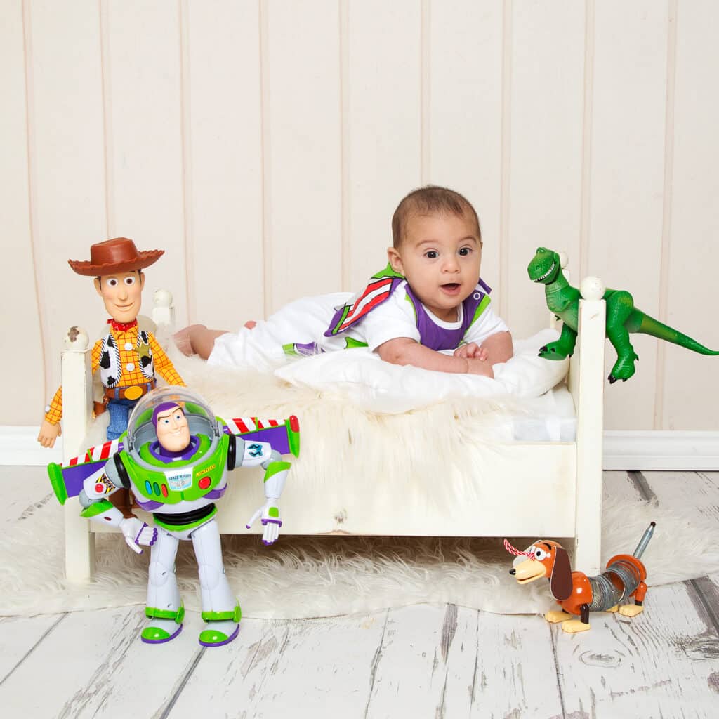 Baby Photography East Grinstead West Sussex a baby on a white bed dressed as Buzz Lightyear with Toy Story toys