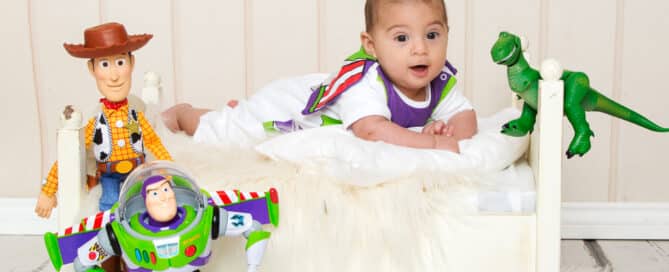 a baby on a white bed dressed as Buzz Lightyear with Toy Story toys