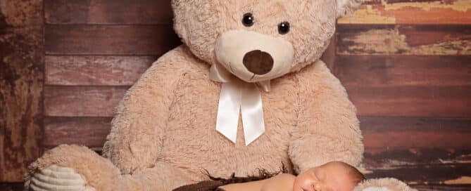 a sleeping newborn lying on the legs of a giant teddy bear