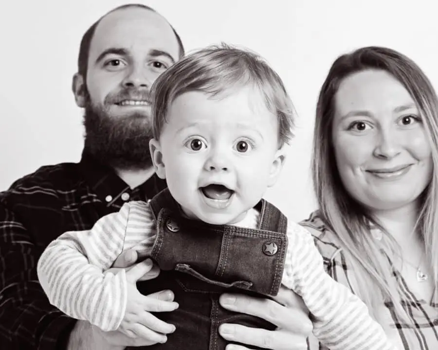 a mum and and dad pose for a professional black and white image flying their baby towards the camera