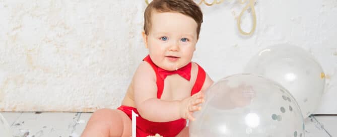 a little boy with a cake and balloons at his first birthday photo shoot