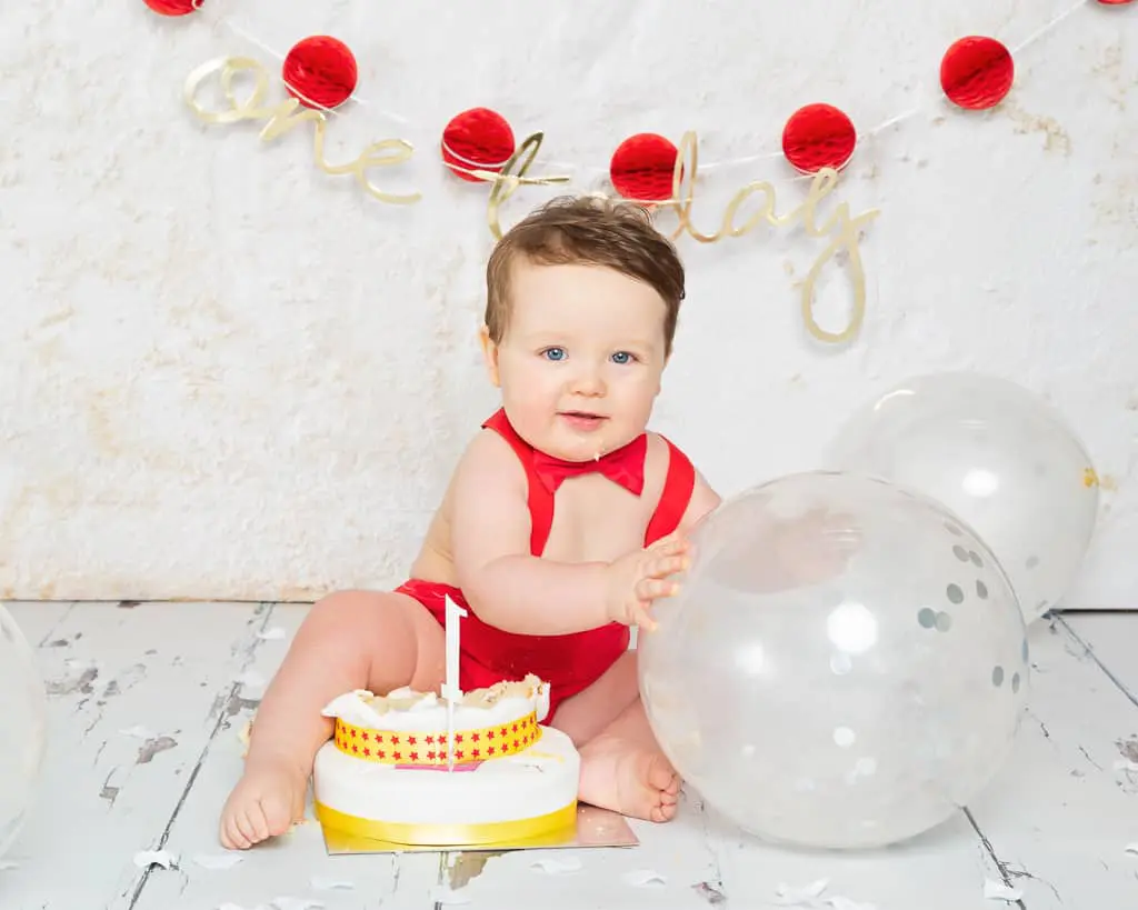 a little boy with a cake and balloons at his first birthday photo shoot