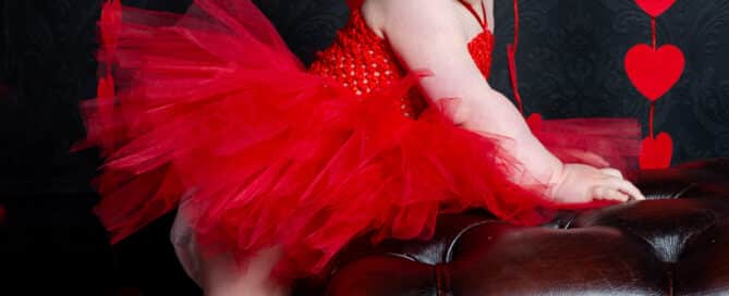 a little girl in a red pettidress poses in front of a curtain of hearts