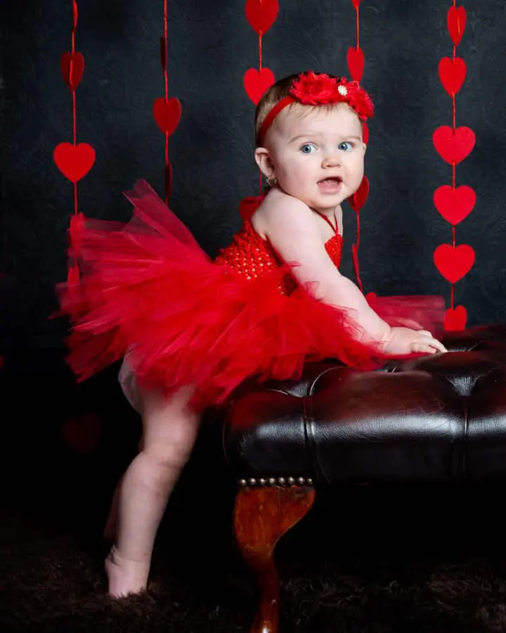 a little girl in a red pettidress poses in front of a curtain of hearts