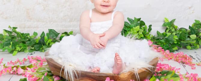 a little girl sits in a bowl surrounded by flowers in a white pettidress