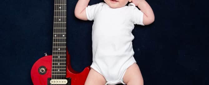 a little boy lies next to his dad's guitar on a navy backdrop