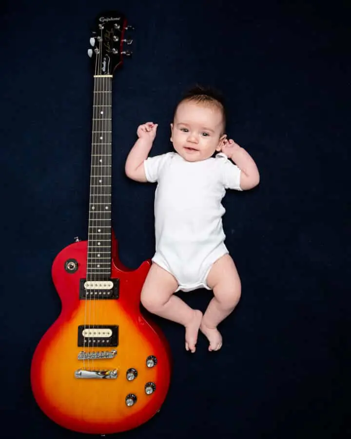 a little boy lies next to his dad's guitar on a navy backdrop