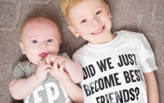 Two children lie on the floor looking up wearing matching tshirts