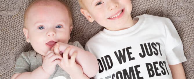 Two children lie on the floor looking up wearing matching tshirts