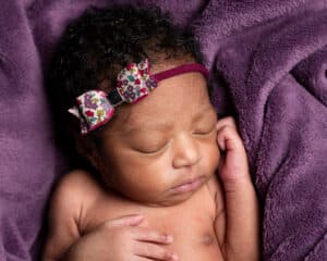 a newborn sleeps on a purple blanket with a purple floral headband