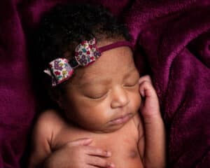 a baby sleeping on a deep purple blanket with a matching headband