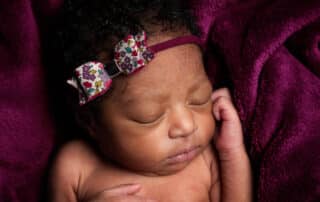 a baby sleeping on a deep purple blanket with a matching headband