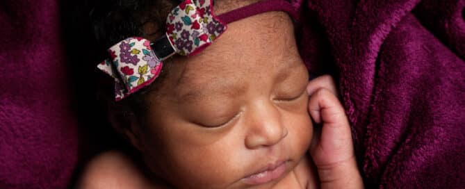 a baby sleeping on a deep purple blanket with a matching headband