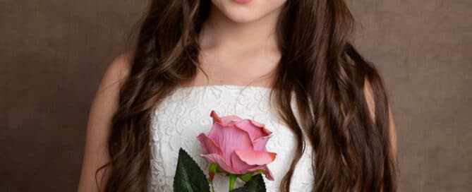 a little girl poses for the camara holding a pink rose