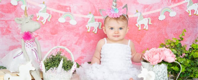 a little girl in a pettidress poses with a unicorn headband and props