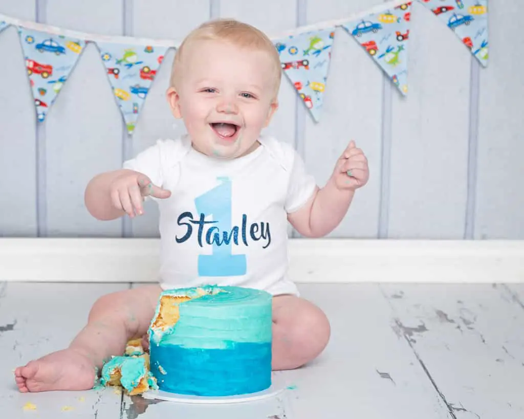 a little boy is laughing as he tucks into his cake at his birthday photo shoot