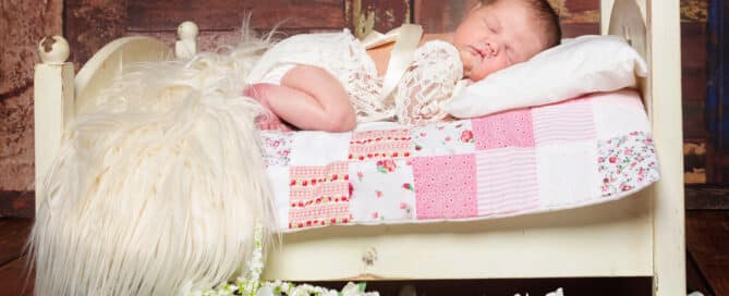 a sleeping baby in a little lace outfit sleeping on a miniature white bed