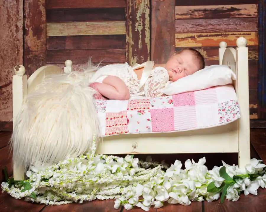 Newborn Photography East Grinstead West Sussex a sleeping baby in a little lace outfit sleeping on a miniature white bed