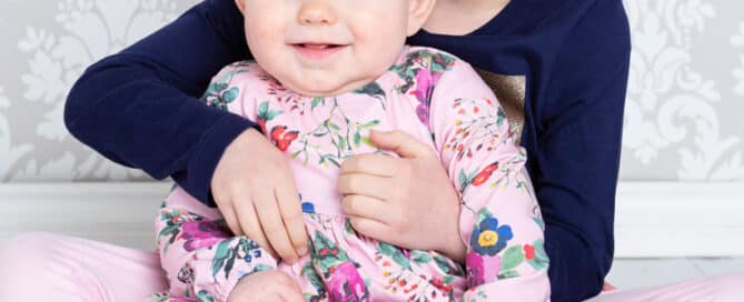 A big sister holds her baby sibling dressed in a floral dress