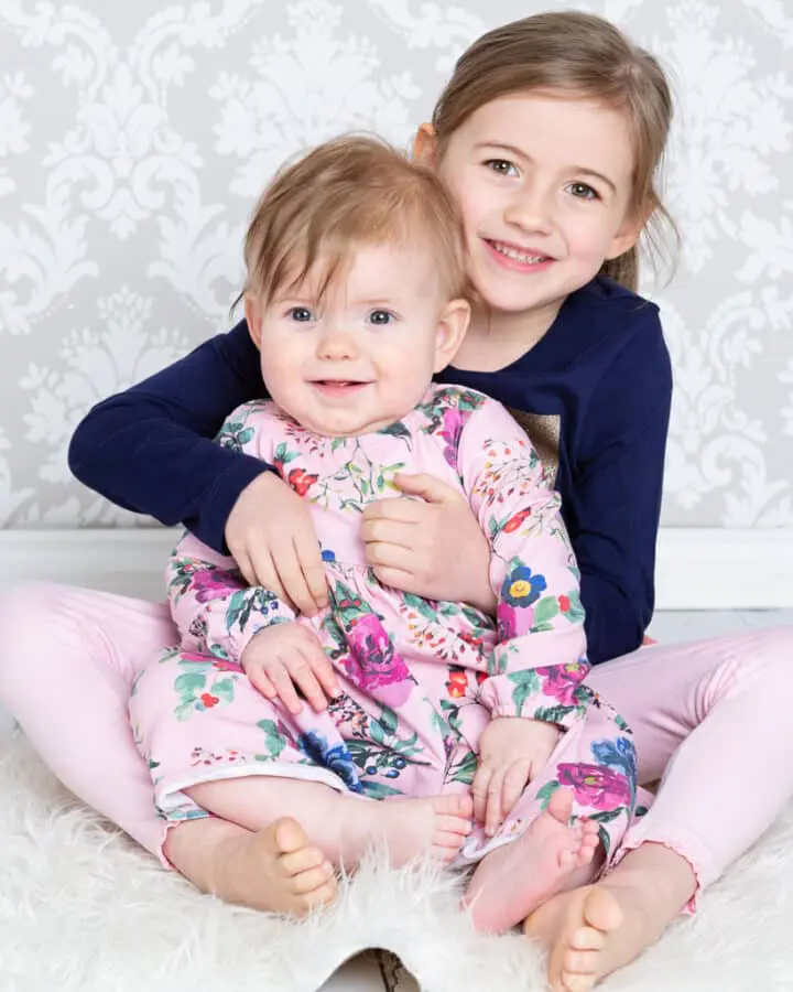 A big sister holds her baby sibling dressed in a floral dress