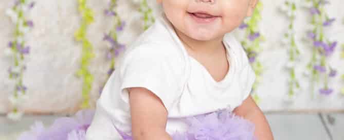 a little girl in a purple tutu poses in front of a lilac flower wall