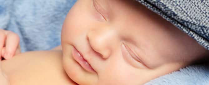 a close up of a newborn baby fast asleep and wearing a flat cap