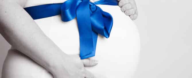 a pregnant lady with a white tshirt on and her bump is wrapped with a blue ribbon.