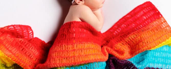 A baby girl sleeping in a rainbow blanket with a rainbow headband
