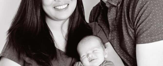 A black and white image of parents holding a newborn and all three of them are smiling for the camera