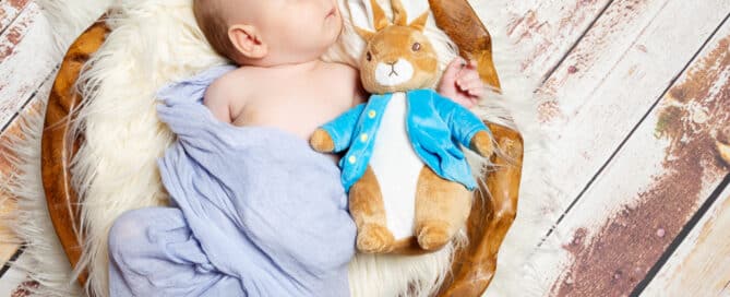 a baby boy newborn sleeping in a wooden bowl with a Peter Rabbit soft toy
