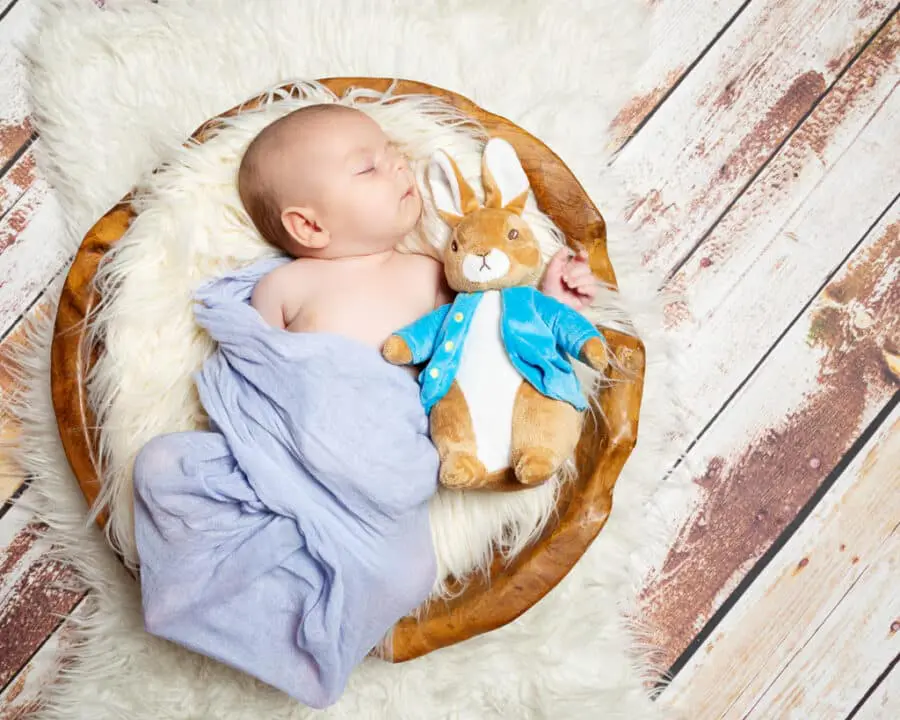 a baby boy newborn sleeping in a wooden bowl with a Peter Rabbit soft toy
