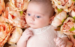 A small baby with their eyes open lying in a nest of peach peonies